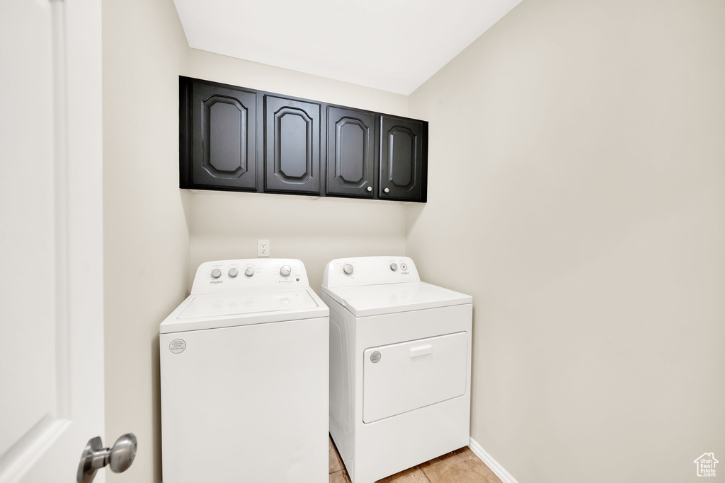 Washroom with light tile patterned flooring, cabinets, and independent washer and dryer