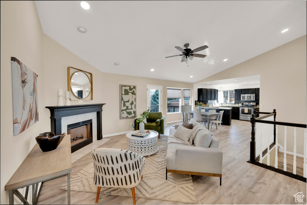 Living room with a tiled fireplace, ceiling fan, light hardwood / wood-style flooring, and lofted ceiling