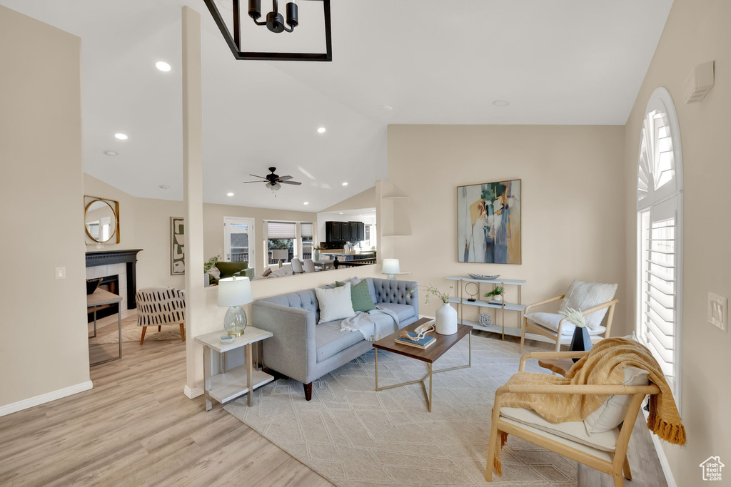 Living room with high vaulted ceiling, ceiling fan, a tile fireplace, and light hardwood / wood-style flooring