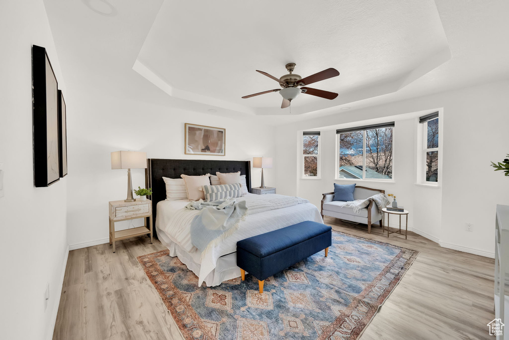 Bedroom with light wood-type flooring, a raised ceiling, and ceiling fan