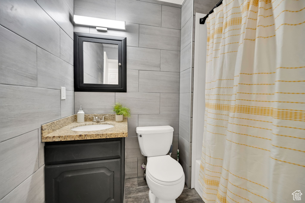 Bathroom with a shower with shower curtain, vanity, toilet, and tile walls