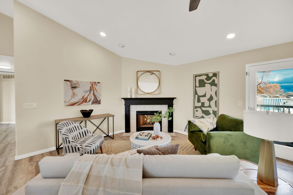 Living room with light wood-type flooring, vaulted ceiling, ceiling fan, and a tiled fireplace