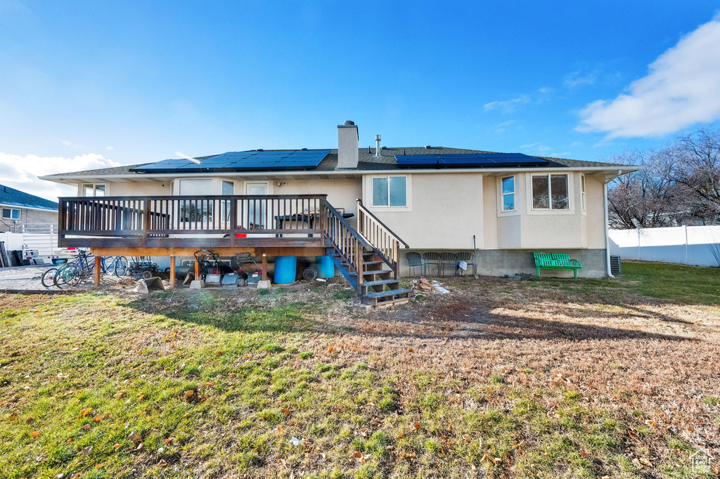 Back of property featuring solar panels, a lawn, and a wooden deck