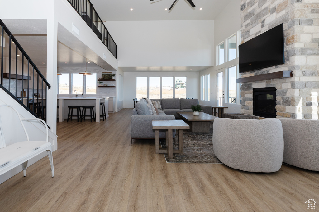 Living room featuring a stone fireplace, light wood-type flooring, a towering ceiling, and a wealth of natural light