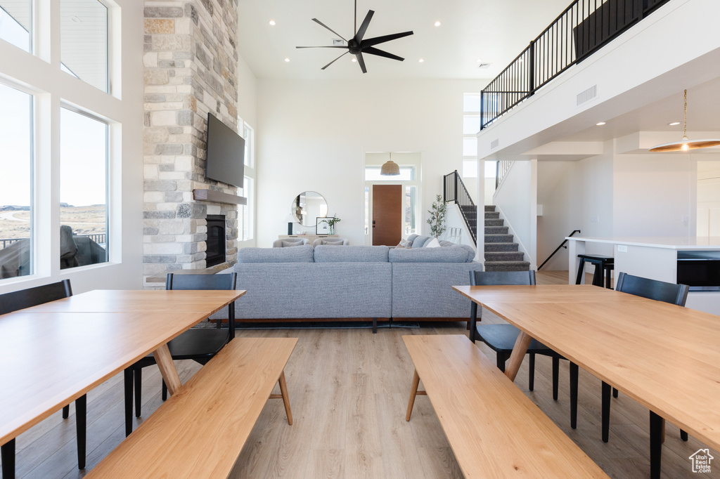 Living room with ceiling fan, light wood-type flooring, a fireplace, and a high ceiling