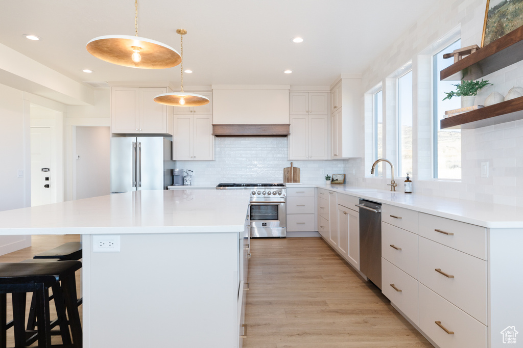 Kitchen featuring sink, hanging light fixtures, high quality appliances, white cabinets, and custom range hood