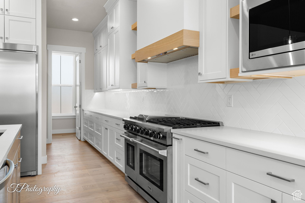 Kitchen featuring high end appliances, custom range hood, light countertops, white cabinetry, and tasteful backsplash