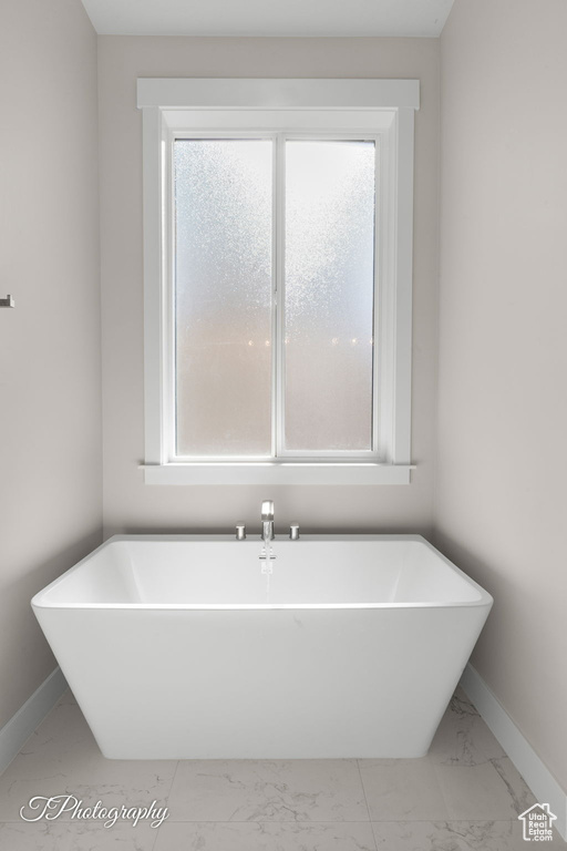 Full bathroom featuring marble finish floors, baseboards, and a freestanding bath