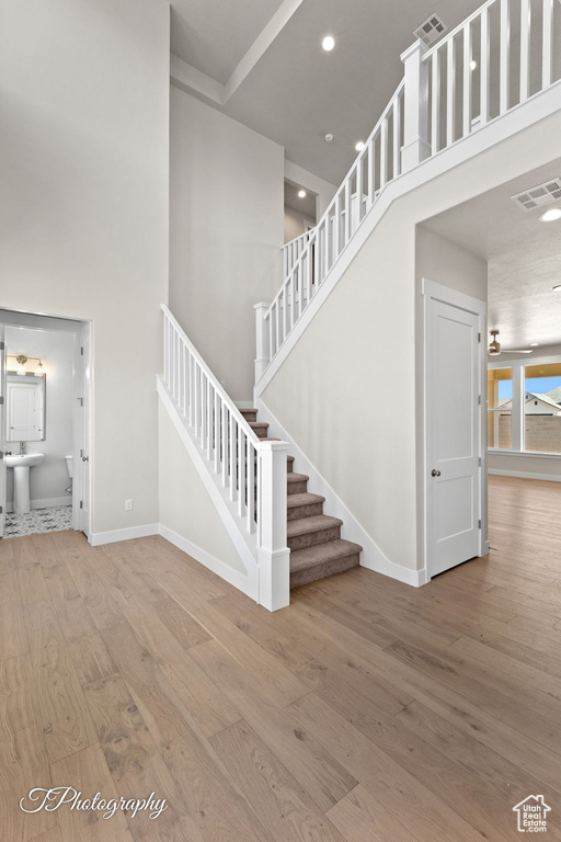 Staircase with a towering ceiling, wood finished floors, baseboards, and recessed lighting