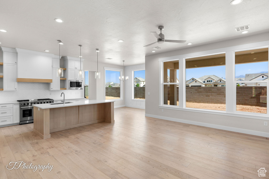Kitchen featuring stainless steel appliances, light countertops, an island with sink, a ceiling fan, and a sink