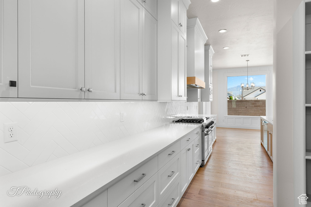Kitchen with high end stainless steel range oven, a chandelier, light countertops, decorative backsplash, and light wood-style floors