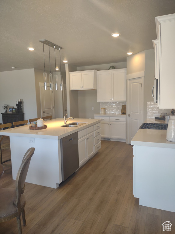 Kitchen featuring stainless steel dishwasher, white cabinetry, dark wood-style floors, tasteful backsplash, and a kitchen island with sink