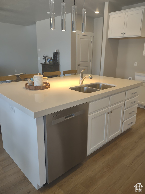 Kitchen with stainless steel dishwasher, wood finished floors, a kitchen island with sink, and white cabinetry
