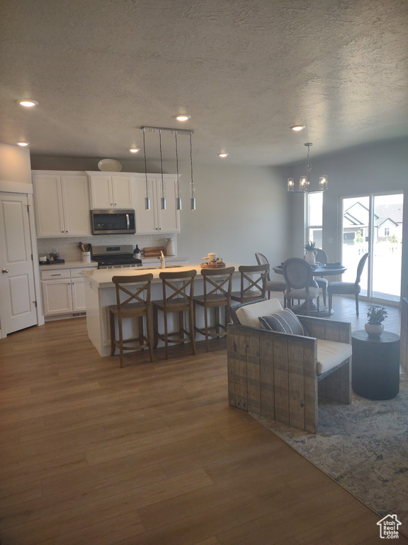 Kitchen with appliances with stainless steel finishes, a textured ceiling, dark wood finished floors, white cabinetry, and backsplash
