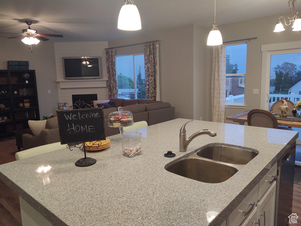 Kitchen featuring ceiling fan with notable chandelier, sink, light stone countertops, a fireplace, and dark hardwood / wood-style flooring