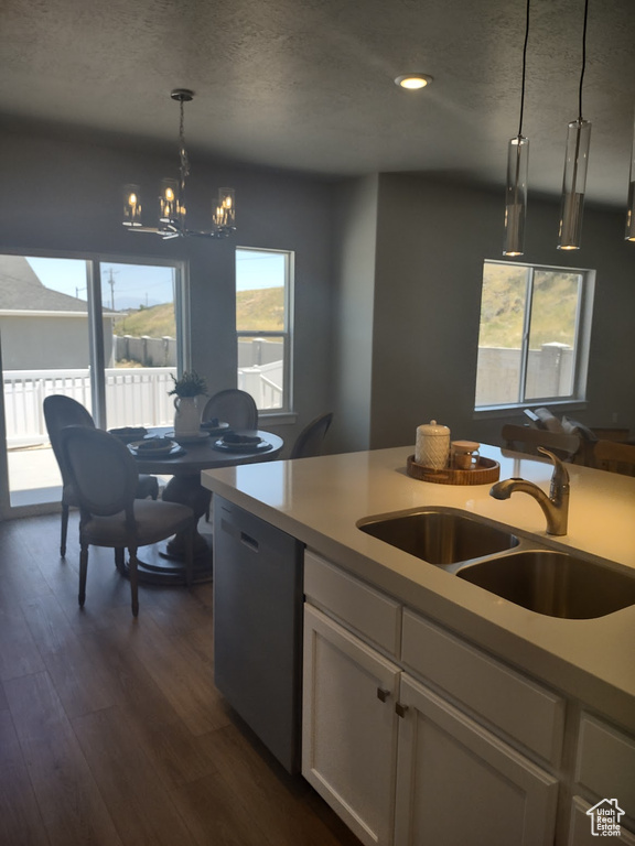 Kitchen with stainless steel dishwasher, a textured ceiling, healthy amount of natural light, a chandelier, and dark wood-style flooring