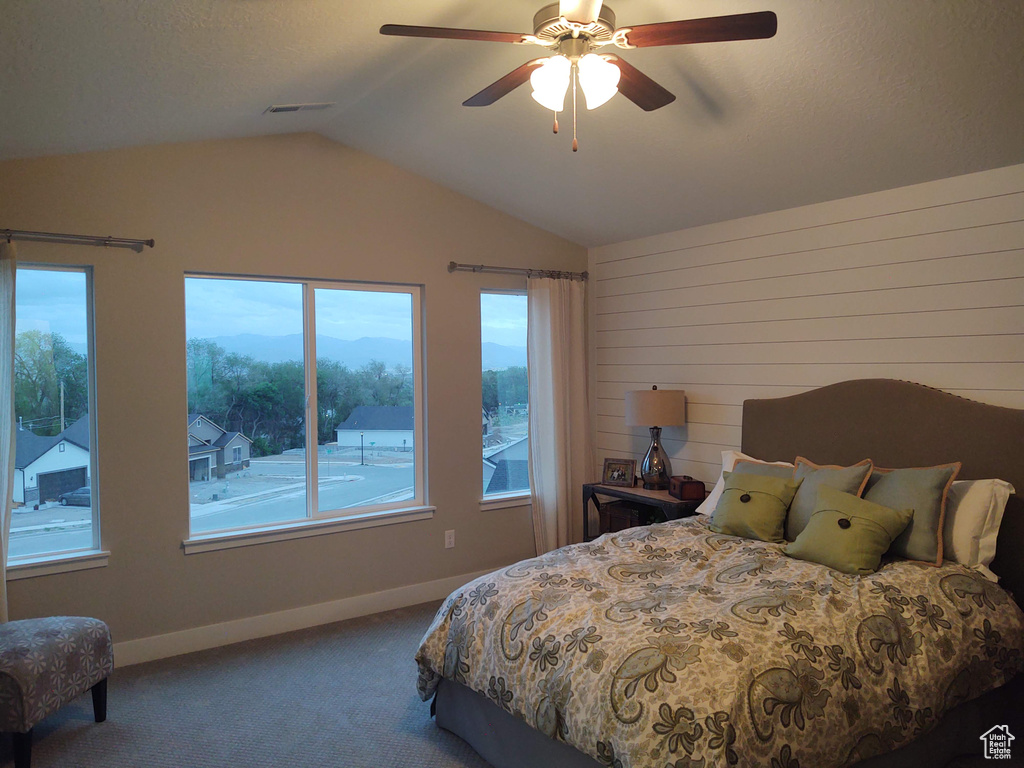 Bedroom with carpet, vaulted ceiling, ceiling fan, and wooden walls