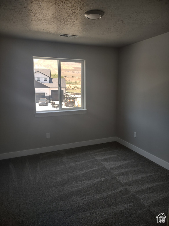 Empty room with dark carpet and a textured ceiling
