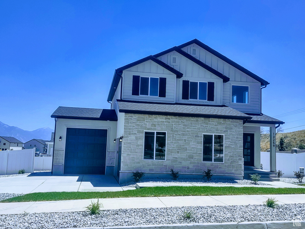 View of front facade featuring stone siding, an attached garage, driveway, board and batten siding, and a mountain view
