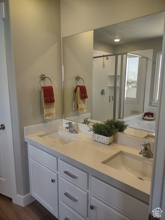 Full bath with a stall shower, double vanity, and wood finished floors