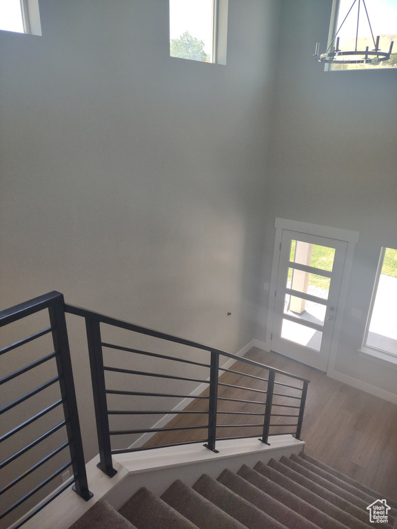 Stairway with wood finished floors, a chandelier, plenty of natural light, and a high ceiling