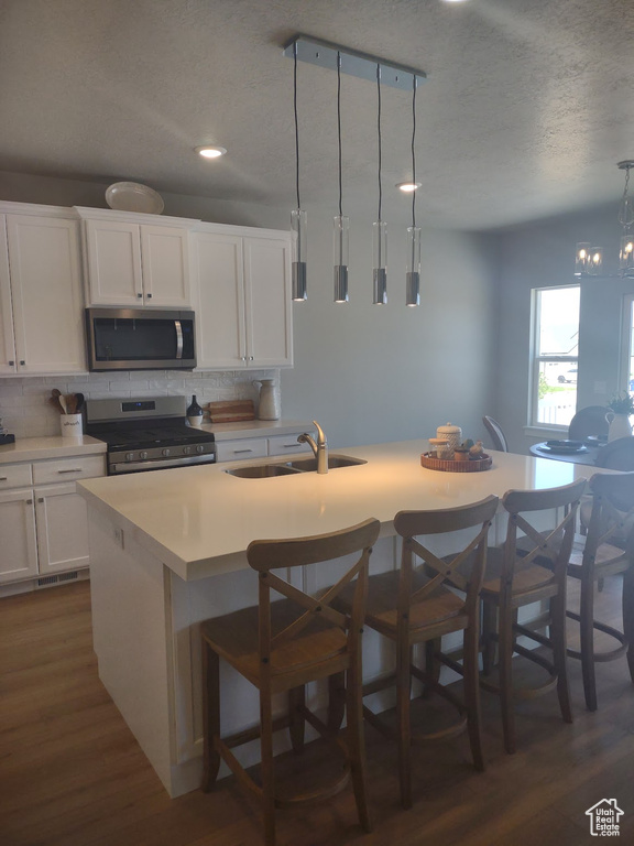 Kitchen featuring appliances with stainless steel finishes, decorative backsplash, dark wood-style flooring, an island with sink, and light countertops