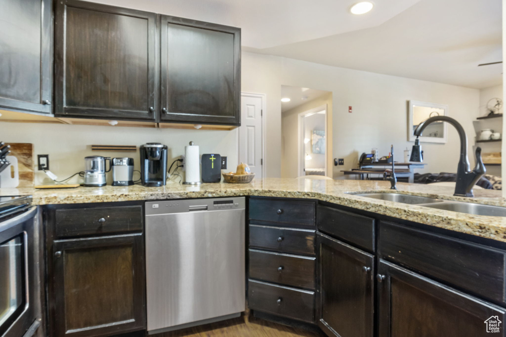 Kitchen featuring sink, appliances with stainless steel finishes, dark brown cabinets, light hardwood / wood-style floors, and light stone counters