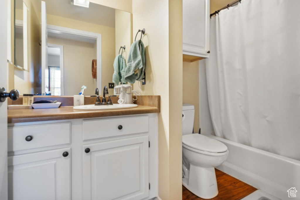 Full bathroom featuring shower / bath combo with shower curtain, vanity, wood-type flooring, and toilet