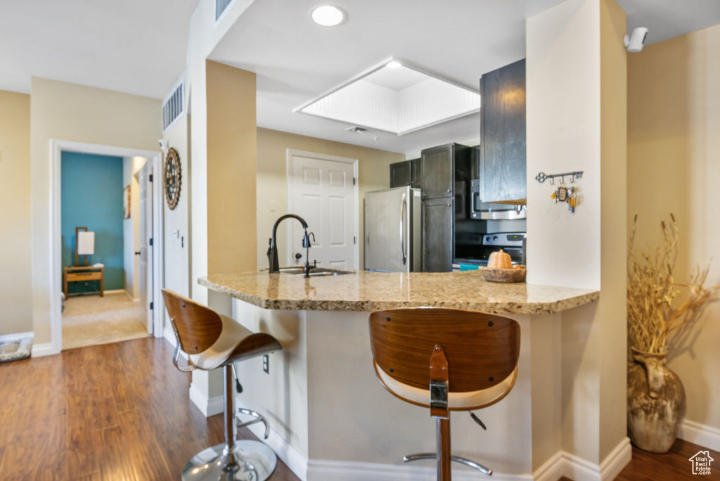 Kitchen featuring kitchen peninsula, dark hardwood / wood-style flooring, a breakfast bar, sink, and stainless steel refrigerator