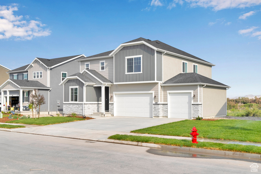 View of front of house featuring a garage, stone siding, driveway, board and batten siding, and a front yard