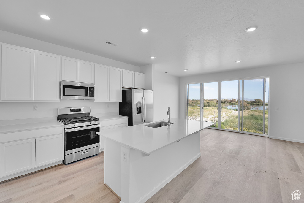 Kitchen featuring stainless steel appliances, a sink, light wood finished floors, white cabinets, and recessed lighting