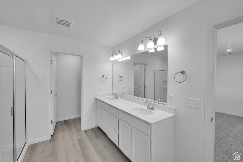 Bathroom featuring double vanity, baseboards, a shower with door, and wood finished floors