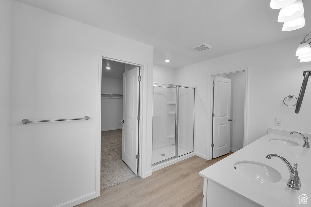 Full bathroom with wood finished floors, a stall shower, a walk in closet, double vanity, and baseboards