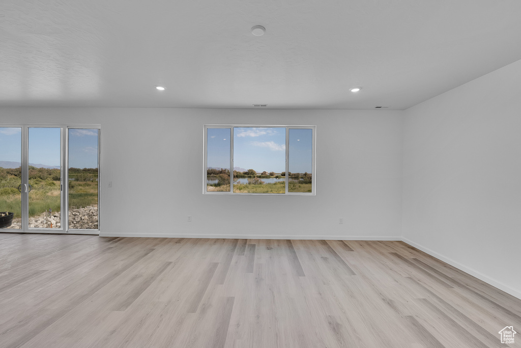 Empty room with healthy amount of natural light, light wood finished floors, recessed lighting, and baseboards