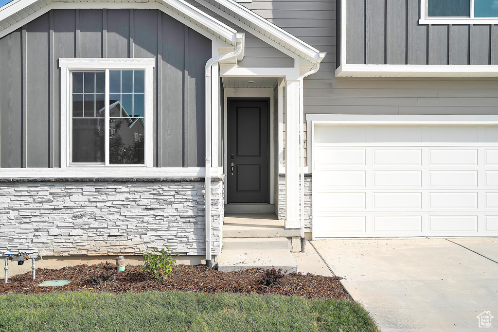 Property entrance featuring stone siding, an attached garage, and concrete driveway