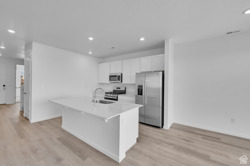 Kitchen with appliances with stainless steel finishes, a sink, recessed lighting, a kitchen island with sink, and white cabinetry