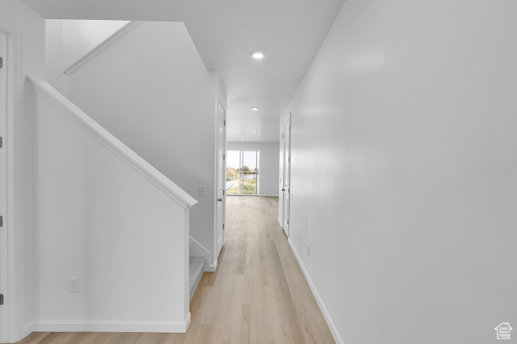 Hall with light wood finished floors, stairway, recessed lighting, and baseboards