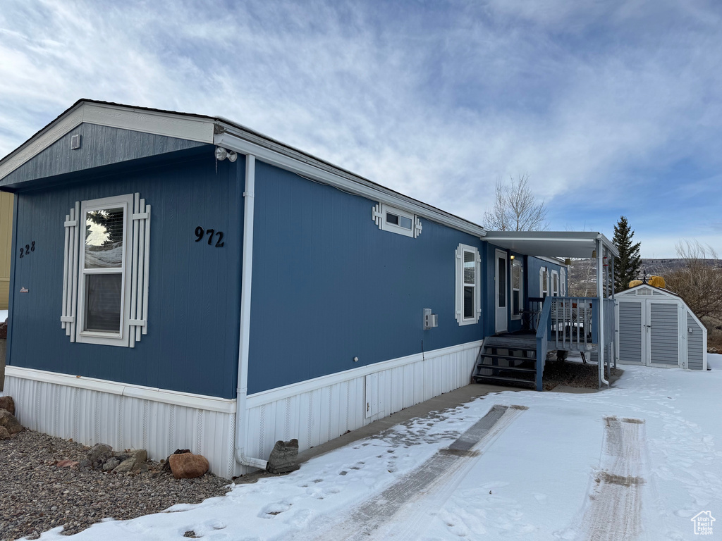 Snow covered property featuring a wooden deck and a storage shed