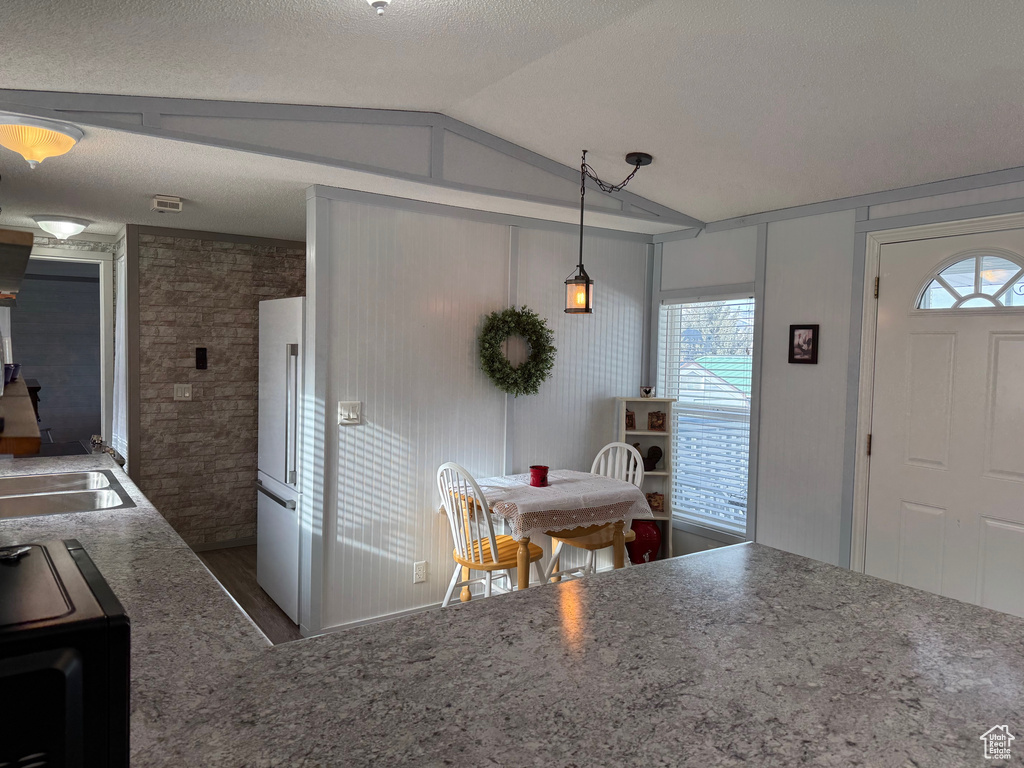 Kitchen featuring pendant lighting, lofted ceiling, dark wood-type flooring, white refrigerator, and a textured ceiling