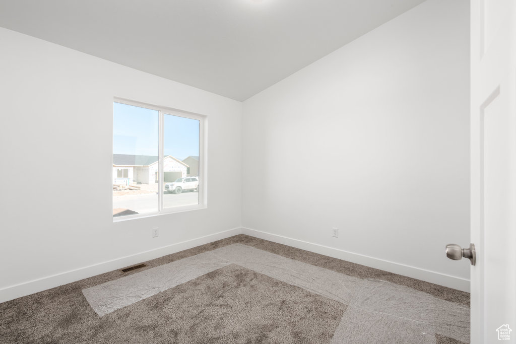 Carpeted empty room featuring vaulted ceiling