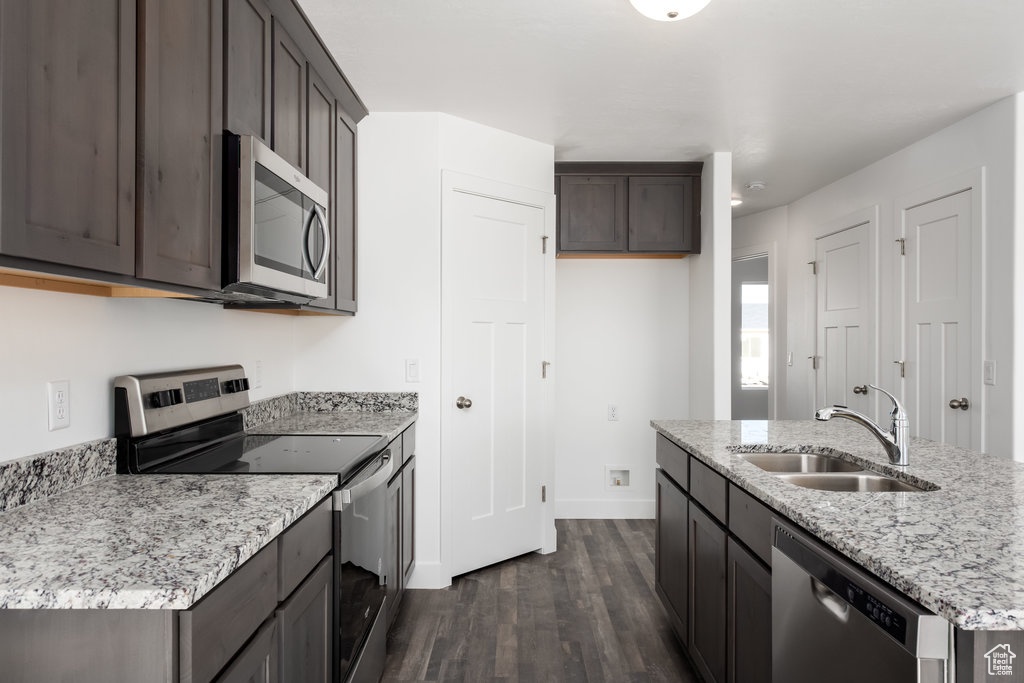 Kitchen with a kitchen island with sink, dark wood-type flooring, sink, light stone countertops, and appliances with stainless steel finishes