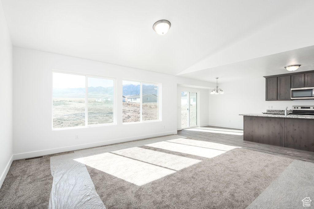 Unfurnished living room featuring carpet, lofted ceiling, sink, and a chandelier