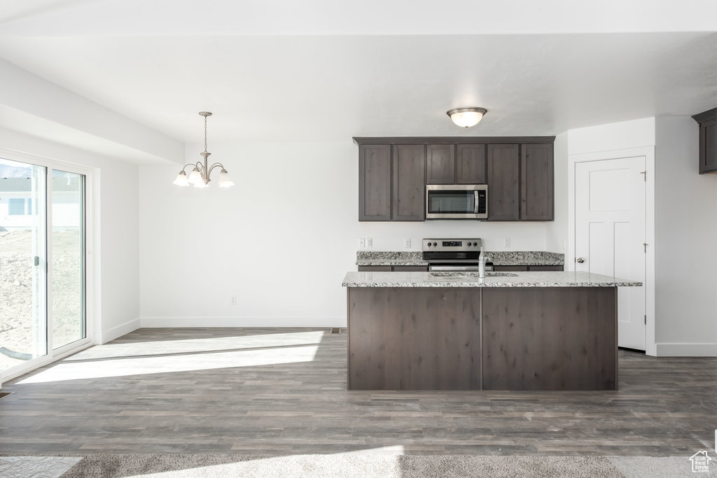 Kitchen with appliances with stainless steel finishes, light stone counters, dark brown cabinets, dark wood-type flooring, and decorative light fixtures