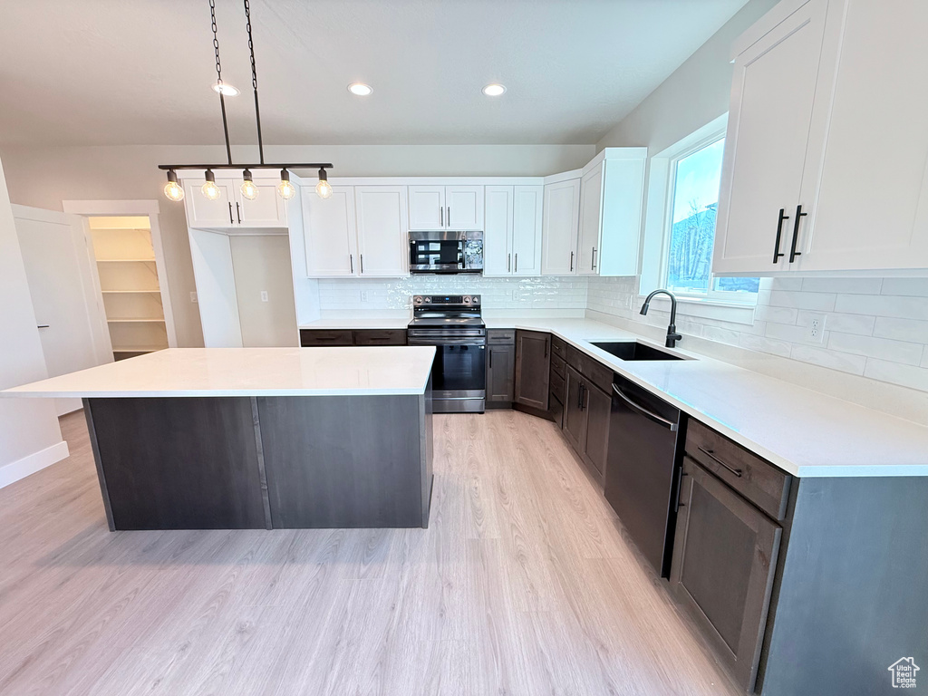 Kitchen with appliances with stainless steel finishes, sink, decorative light fixtures, white cabinets, and a center island