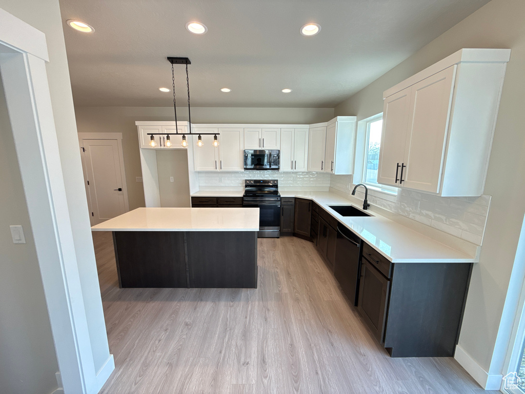 Kitchen with sink, a kitchen island, decorative light fixtures, white cabinets, and appliances with stainless steel finishes