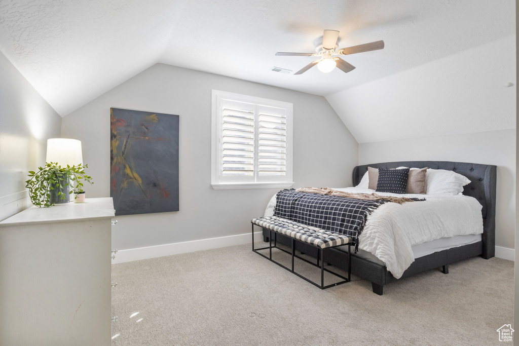 Bedroom with light carpet, a textured ceiling, vaulted ceiling, and ceiling fan