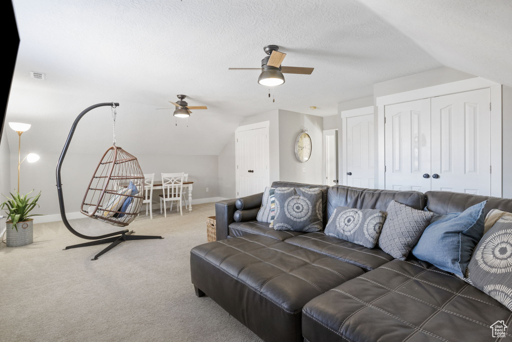 Carpeted living room with a textured ceiling, ceiling fan, and vaulted ceiling