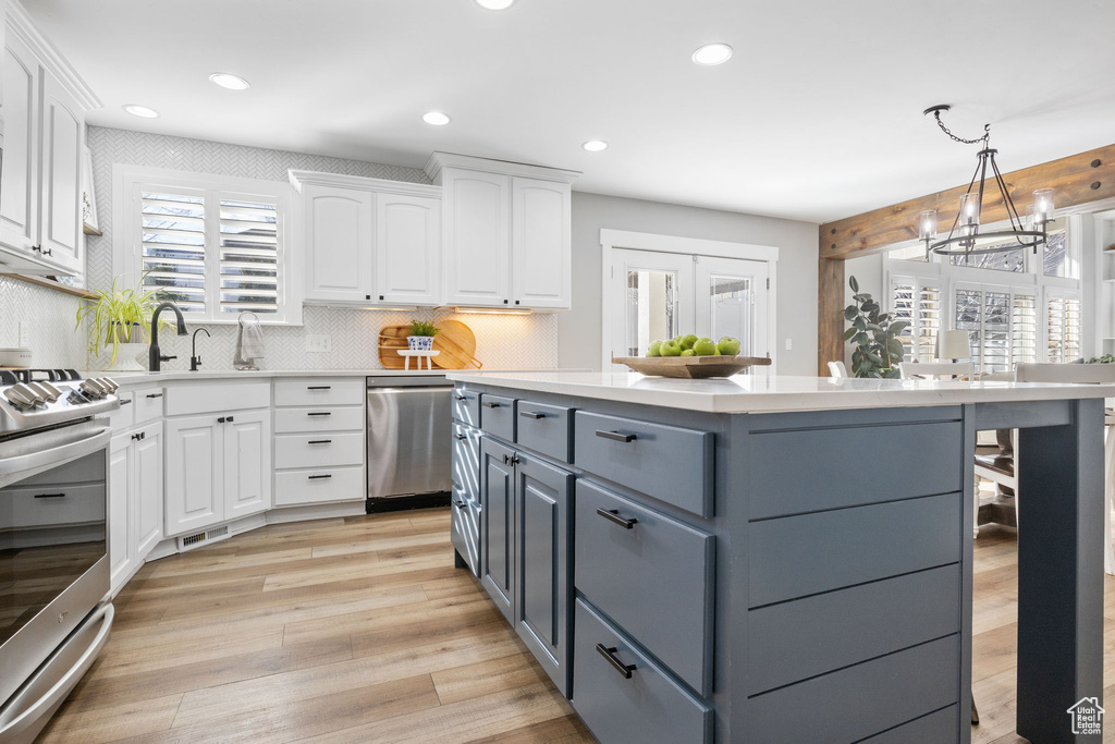 Kitchen with pendant lighting, light wood-type flooring, stainless steel appliances, and white cabinetry