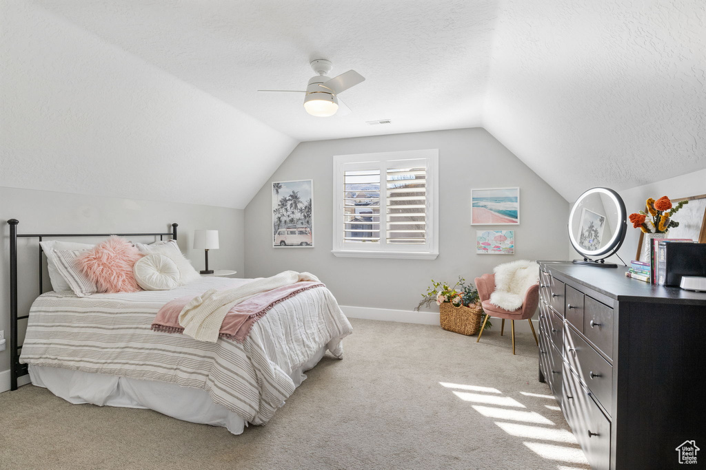 Carpeted bedroom with a textured ceiling, vaulted ceiling, and ceiling fan