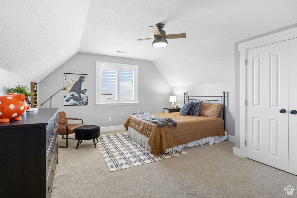 Carpeted bedroom featuring ceiling fan, lofted ceiling, and a textured ceiling